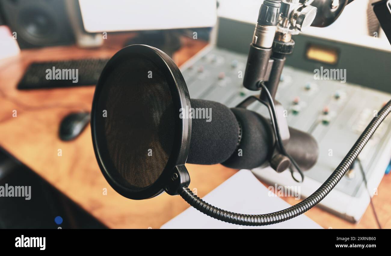 Microphone de studio d'enregistrement professionnel avec filtre pop, prêt pour l'enregistrement de podcast ou vocal. Équipement de production audio de haute qualité sur un bureau en bois, arrière-plan flou du mixeur sonore. Banque D'Images