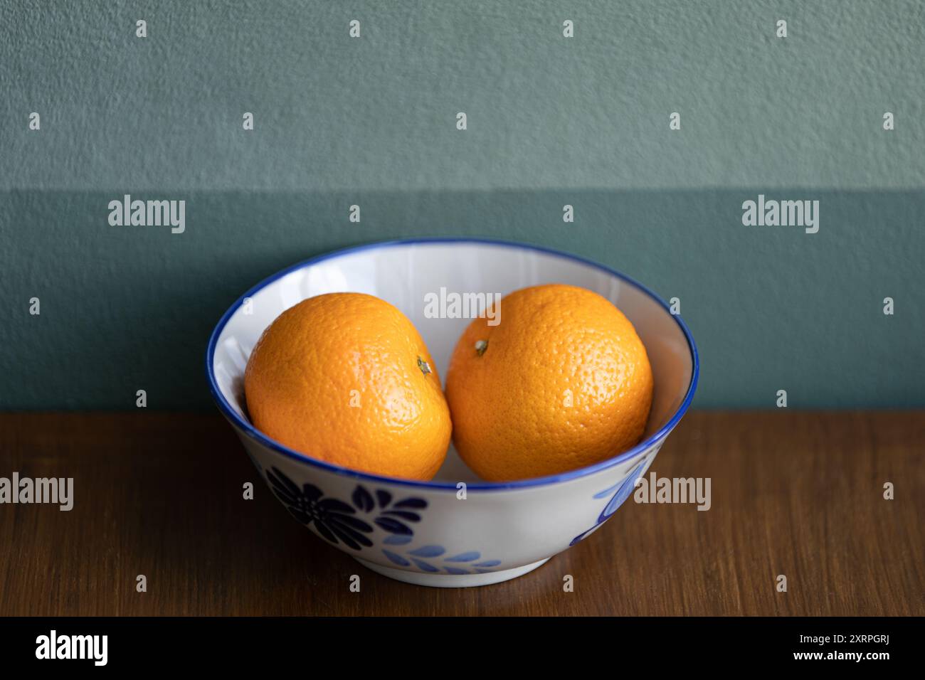 Deux fruits d'oranges sur un bol en céramique blanche sur la table en teck brun, mur vert foncé en arrière-plan. Banque D'Images