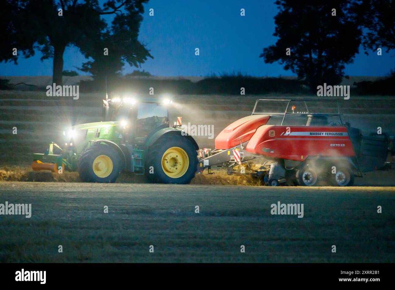 Les agriculteurs travaillent tard dans la nuit pour récolter la récolte début août. Les agriculteurs utilisent des lumières puissantes sur leurs tracteurs pour pouvoir récolter tard dans la soirée. La ferme est située dans le Warwickshire rural, dans les Midlands, Royaume-Uni. Banque D'Images