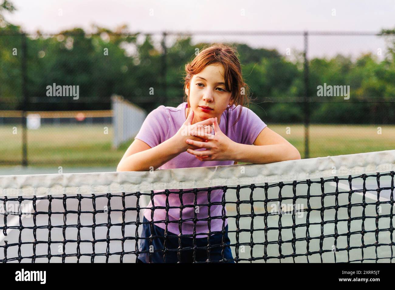 Portrait d'une fille réfléchie penchée sur le filet au court de tennis Banque D'Images
