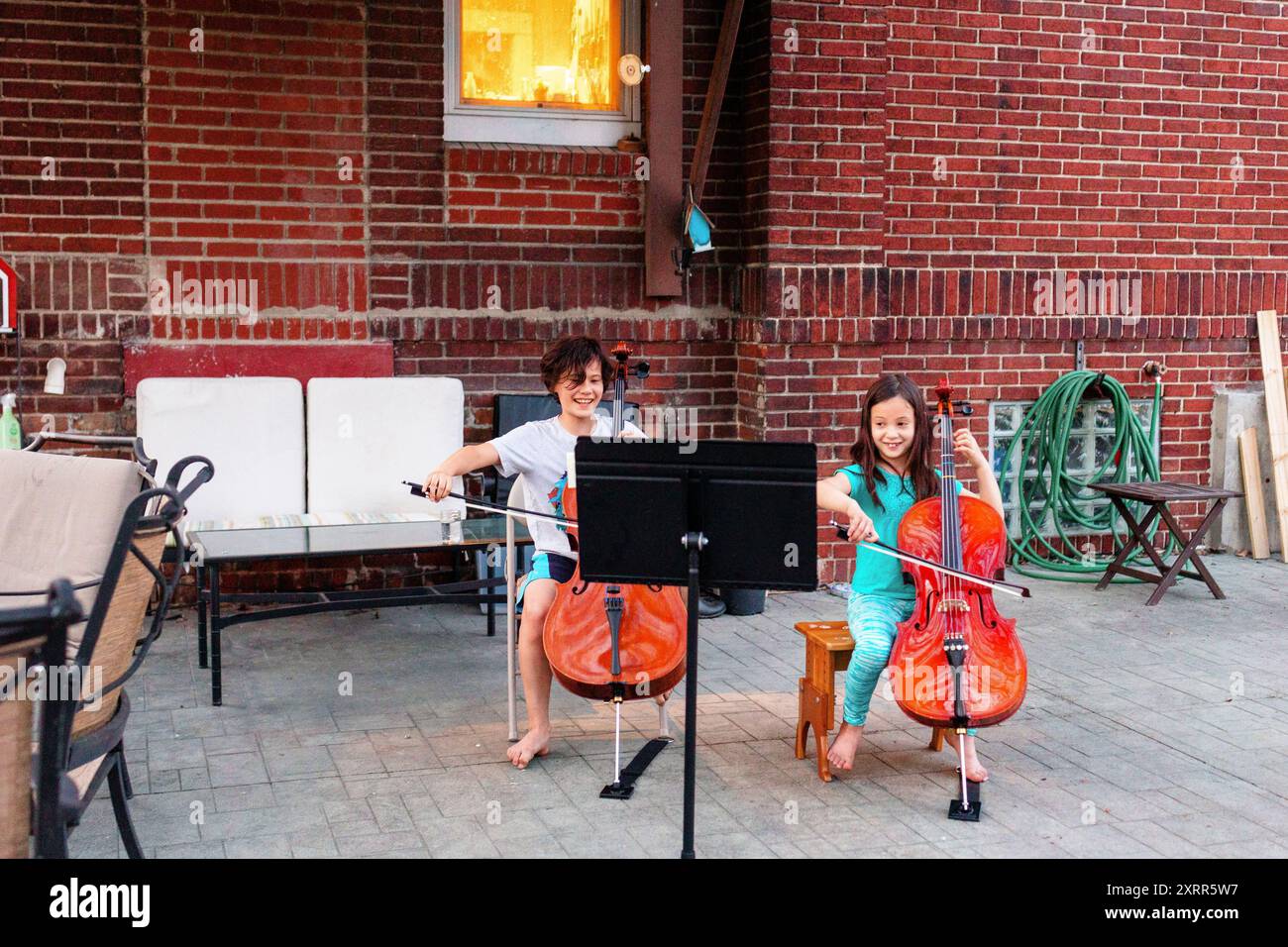 Deux enfants souriants jouent au violoncelle ensemble sur le patio de la maison Banque D'Images