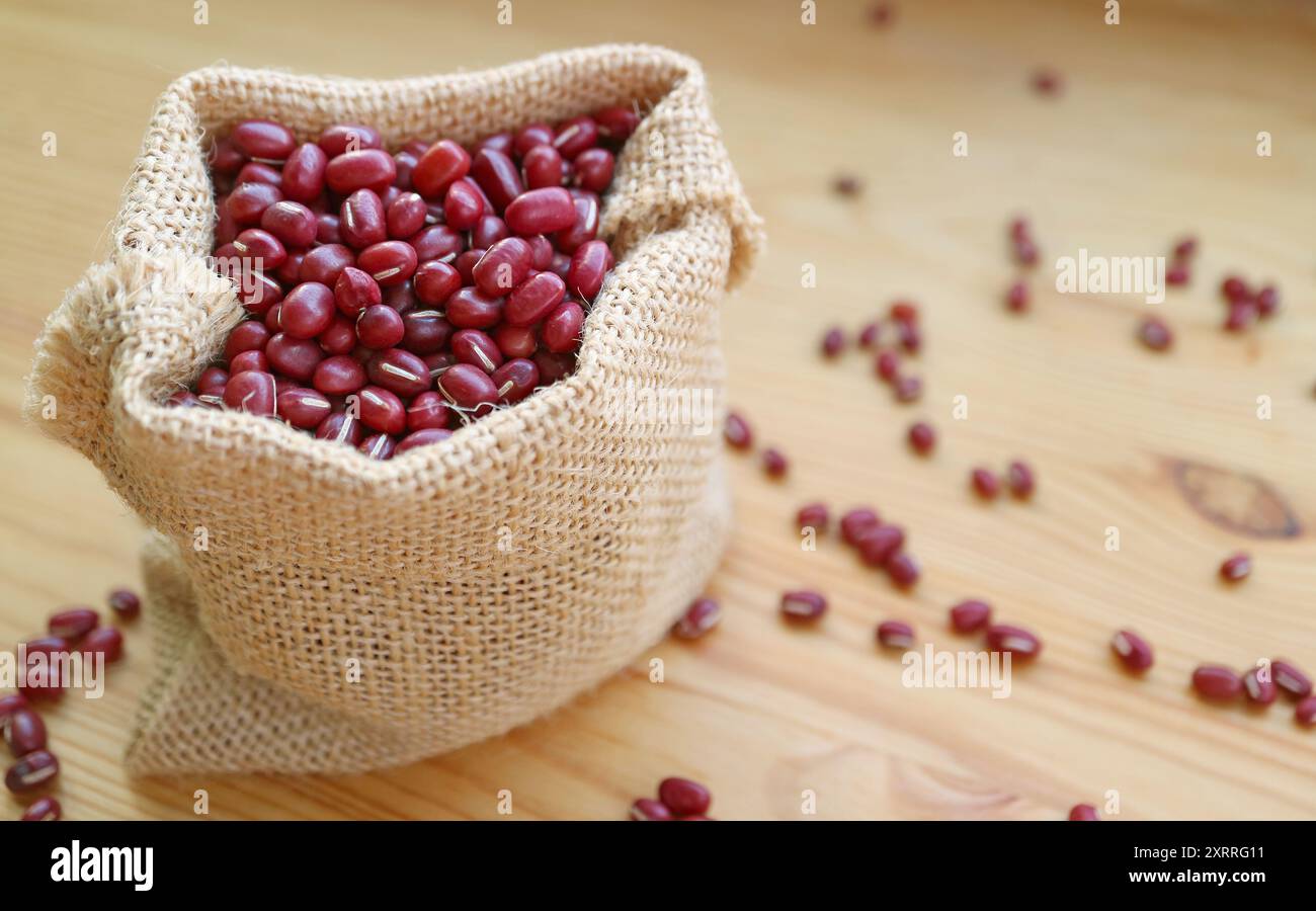 Gros plan de haricots rouges Adzuki séchés dans un sac en toile de jute isolé sur une table en bois Banque D'Images