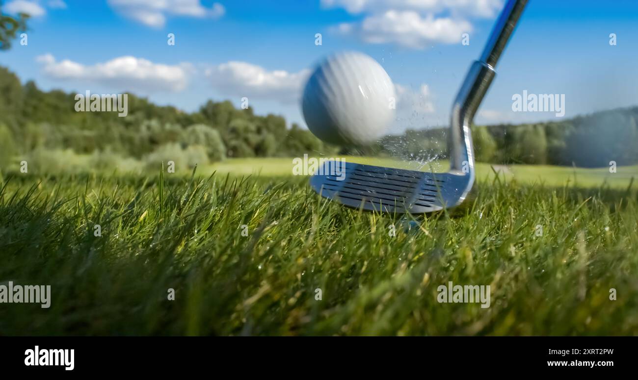 Un club de golf frappe une balle de golf. Des gouttes de rosée matinale et de particules d'herbe s'élèvent dans l'air après l'impact. Banque D'Images
