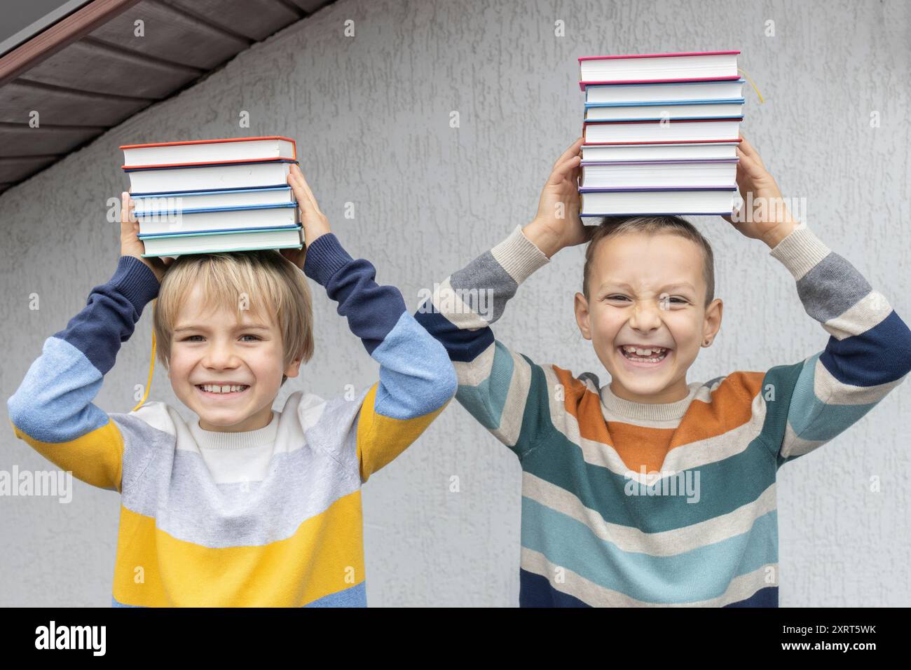 Deux frères ou amis de 7-8 ans tiennent des piles de livres sur leur tête. retour à l'école. Livre Day. concept de lecture, d'éducation, de connaissance. Numérique Banque D'Images