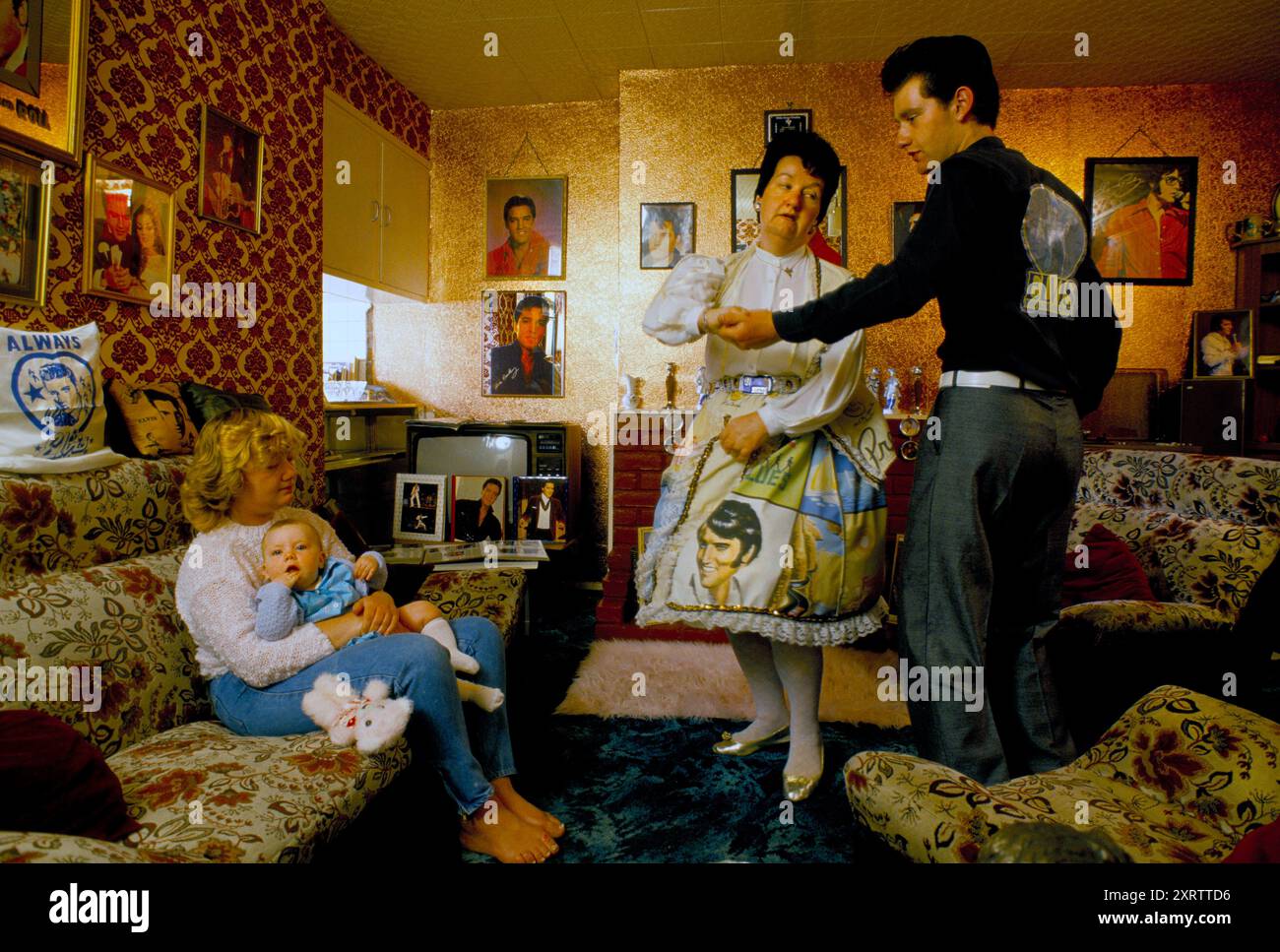 Elvis Presley famille de fans, Mme Debbie Constable et sa fille Lisa Marie Holding fille. Elle porte le nom de la fille unique de Presley, Lisa Marie Presley. Mme Constable dansant avec Chris son beau-fils pour Elvis enregistre dans le salon de leur maison du sud de Londres. Mme Constable porte une robe imprimée Elvis et des boucles d'oreilles portrait Elvis. Photos du roi du Rock and Roll -Elvis Presley décorer l'intérieur des appartements. Tooting, South London, Angleterre vers les années 1995 1990 Royaume-Uni HOMER SYKES Banque D'Images