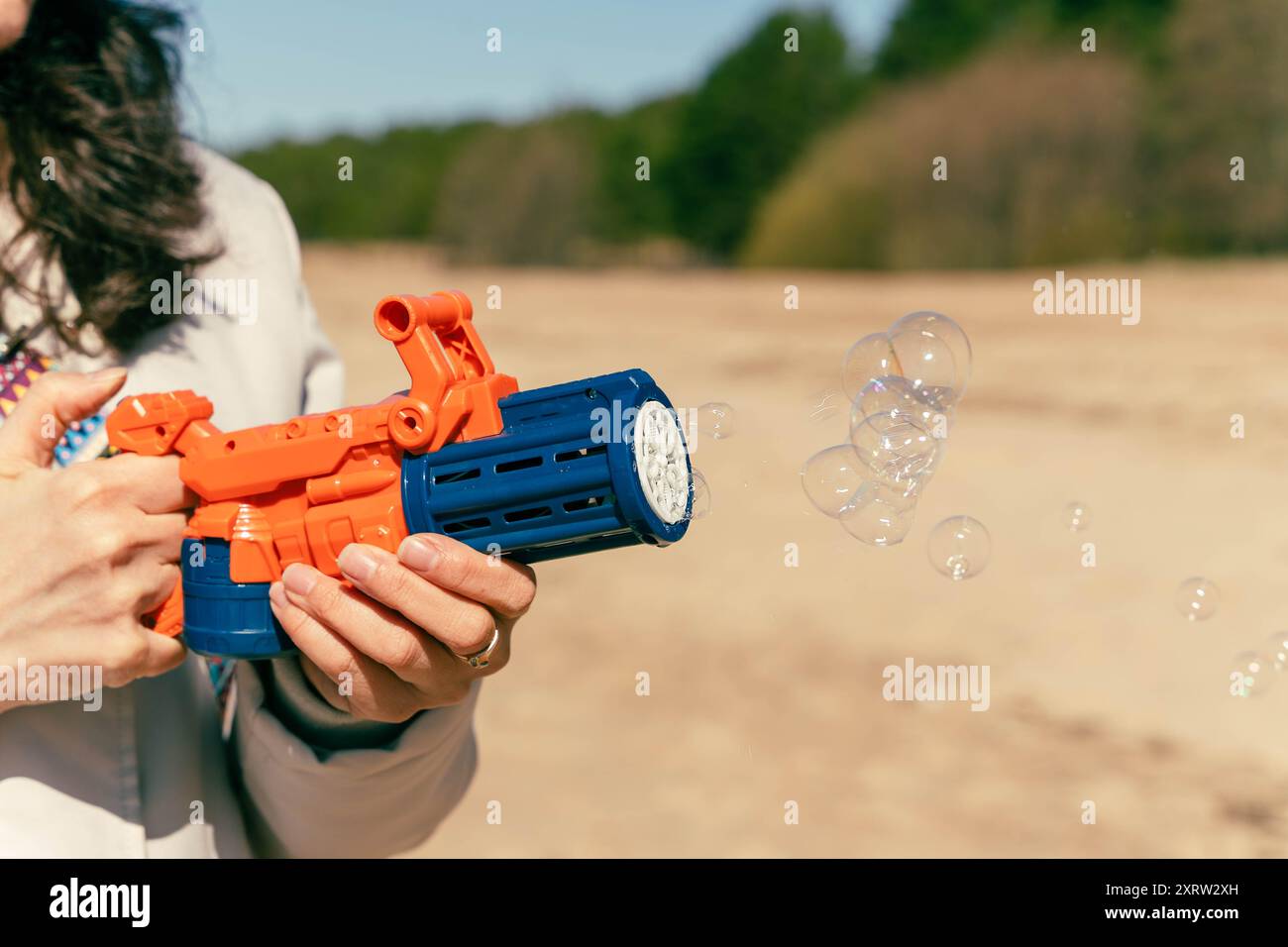 Femme joyeusement tenant et visant un pistolet nerf à l'extérieur par une journée ensoleillée. Banque D'Images