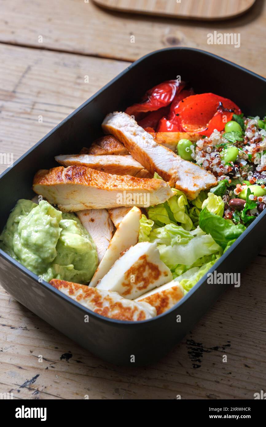 Une boîte à lunch en plastique avec trempette à l'avocat, salade ffresh, haloumi grillé et lanières de poulet. Banque D'Images