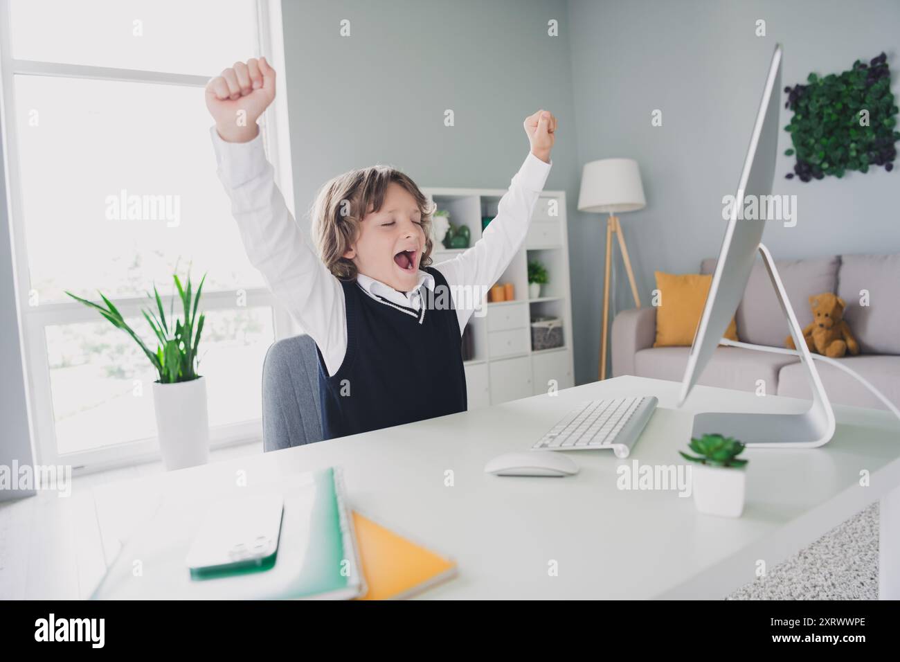 Portrait de fatigué mignon apprenant amusant garçon assis chaise de bureau écouter la leçon vidéo d'ordinateur à l'intérieur de la salle matin Banque D'Images