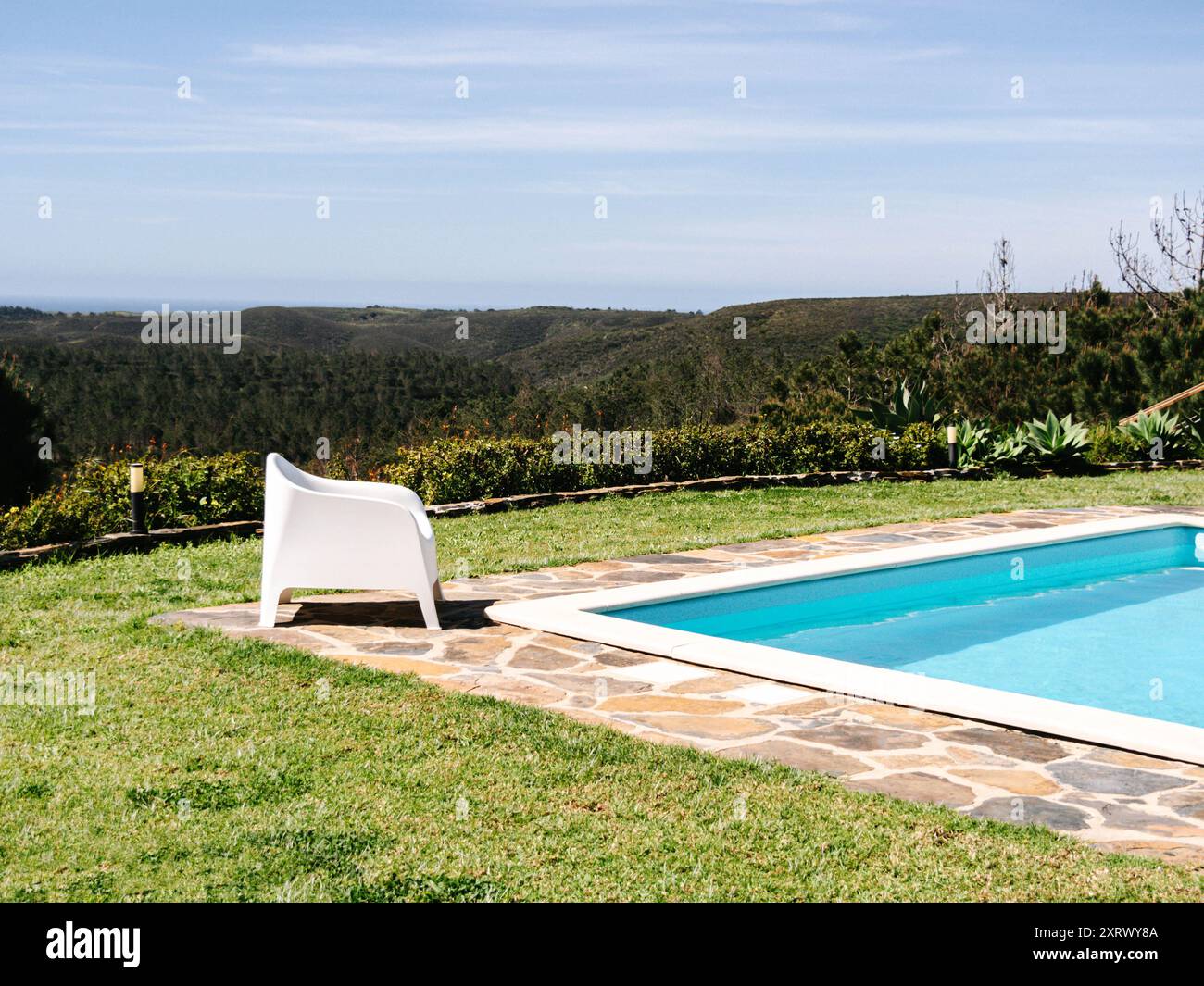 Un cadre serein au bord de la piscine avec des chaises longues blanches donnant sur une vue panoramique sur les montagnes luxuriantes sous un vaste ciel Banque D'Images