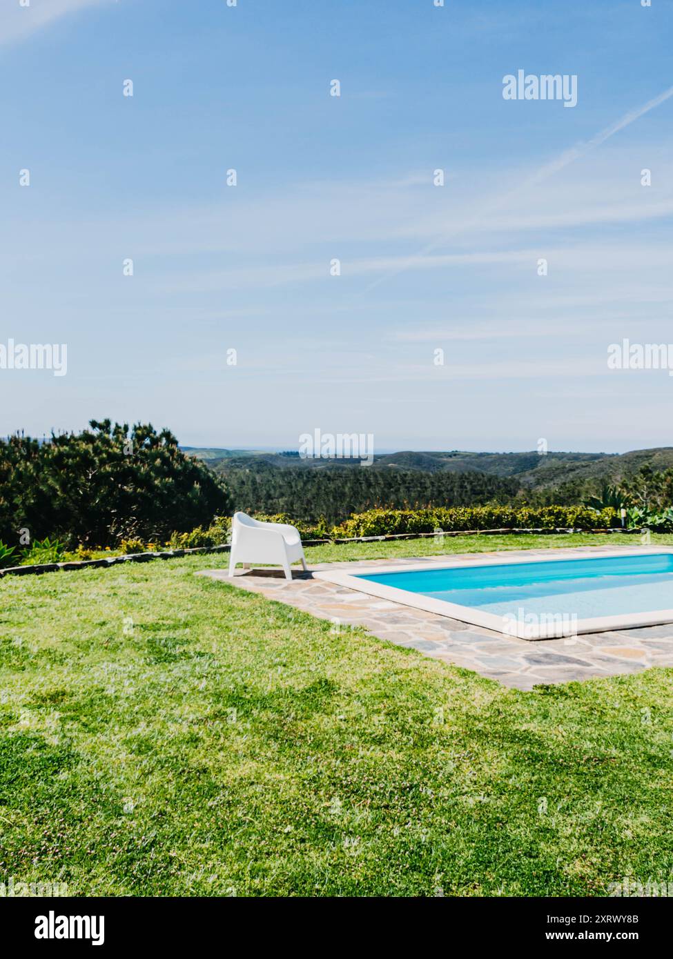 Un cadre serein au bord de la piscine avec des chaises longues blanches donnant sur une vue panoramique sur les montagnes luxuriantes sous un vaste ciel Banque D'Images