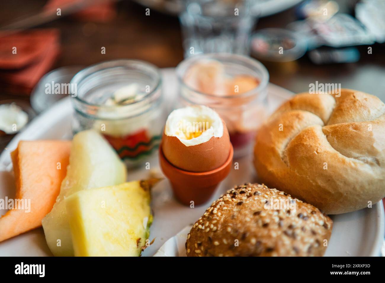 Oeuf bouilli craqué ouvrir sur une assiette de petit déjeuner avec des petits pains et des tranches de fruits Banque D'Images