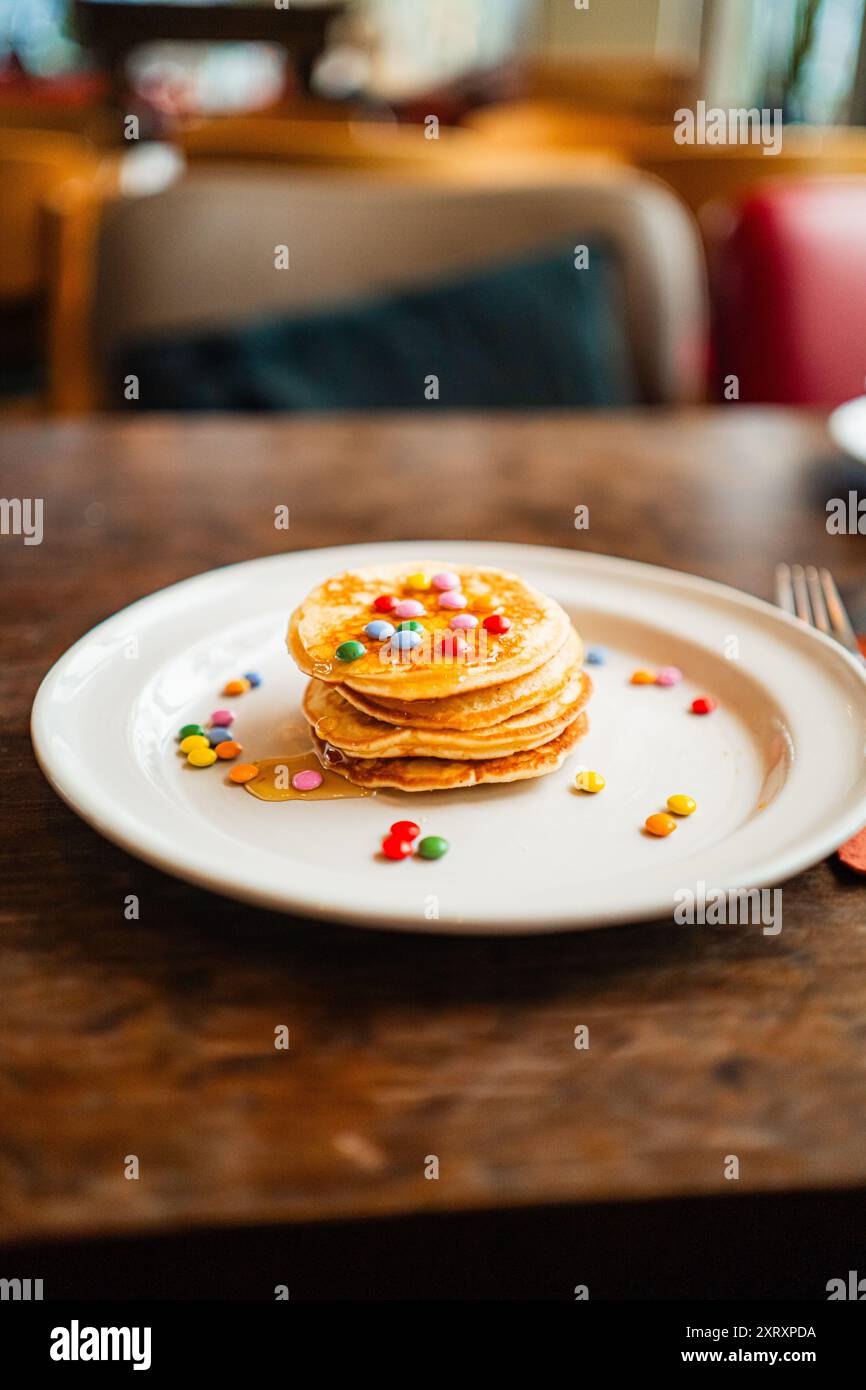 Assiette de petit déjeuner avec une petite pile de crêpes brillantes recouverte de lentille au chocolat et de miel d'abeille Banque D'Images