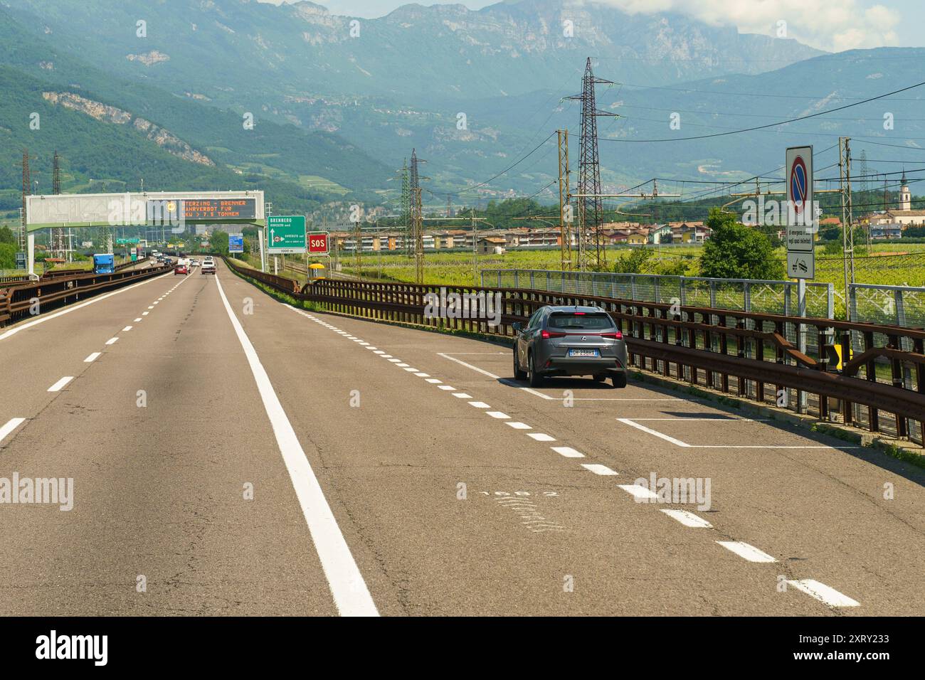 Lizzana, Italie - 8 juin 2023 : une voiture stationne sur le côté de l'autoroute, affichant un panneau SOS, entourée de champs luxuriants et d'une montagne imposante Banque D'Images