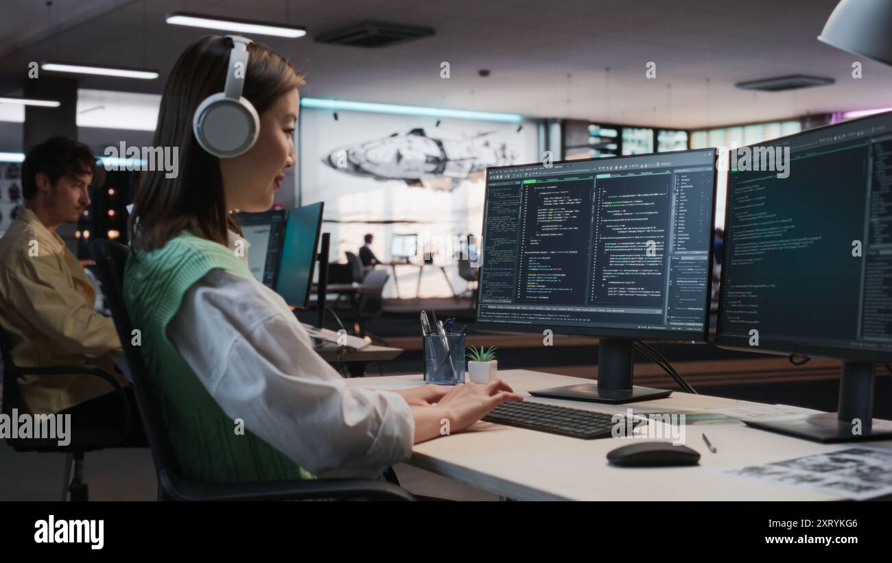 Programmeur de jeu asiatique féminin codage sur ordinateur de bureau dans Game Development Studio diverse Office. Focused Woman écrit des lignes de code, fait de l'ingénierie de gameplay pour le nouveau jeu vidéo RPG immersif 3D. Banque D'Images