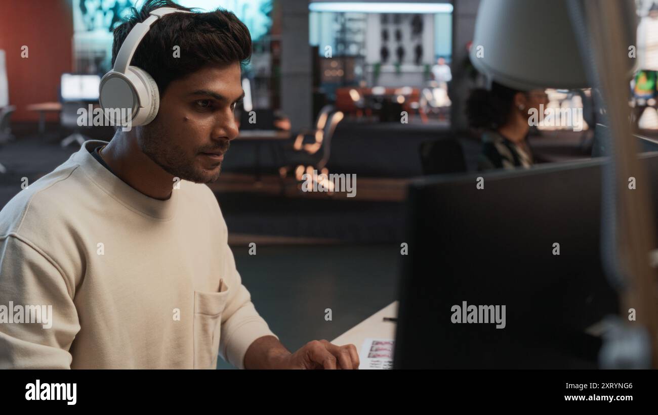 Programmeur de jeu indien masculin codage sur ordinateur de bureau dans Game Design Studio diverse Office. Focused Man écrit des lignes de code, fait de l'ingénierie de gameplay pour le nouveau jeu vidéo de survie immersive 3D. Banque D'Images