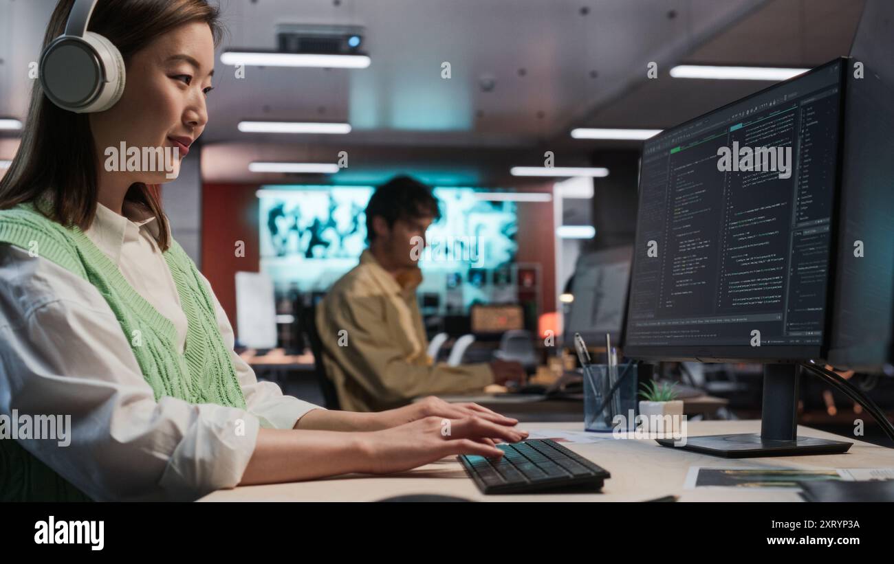 Programmeur de jeu asiatique féminin codage sur ordinateur de bureau dans Game Development Studio diverse Office. Focused Woman écrit des lignes de code, fait de l'ingénierie de gameplay pour le nouveau jeu vidéo RPG immersif 3D. Banque D'Images
