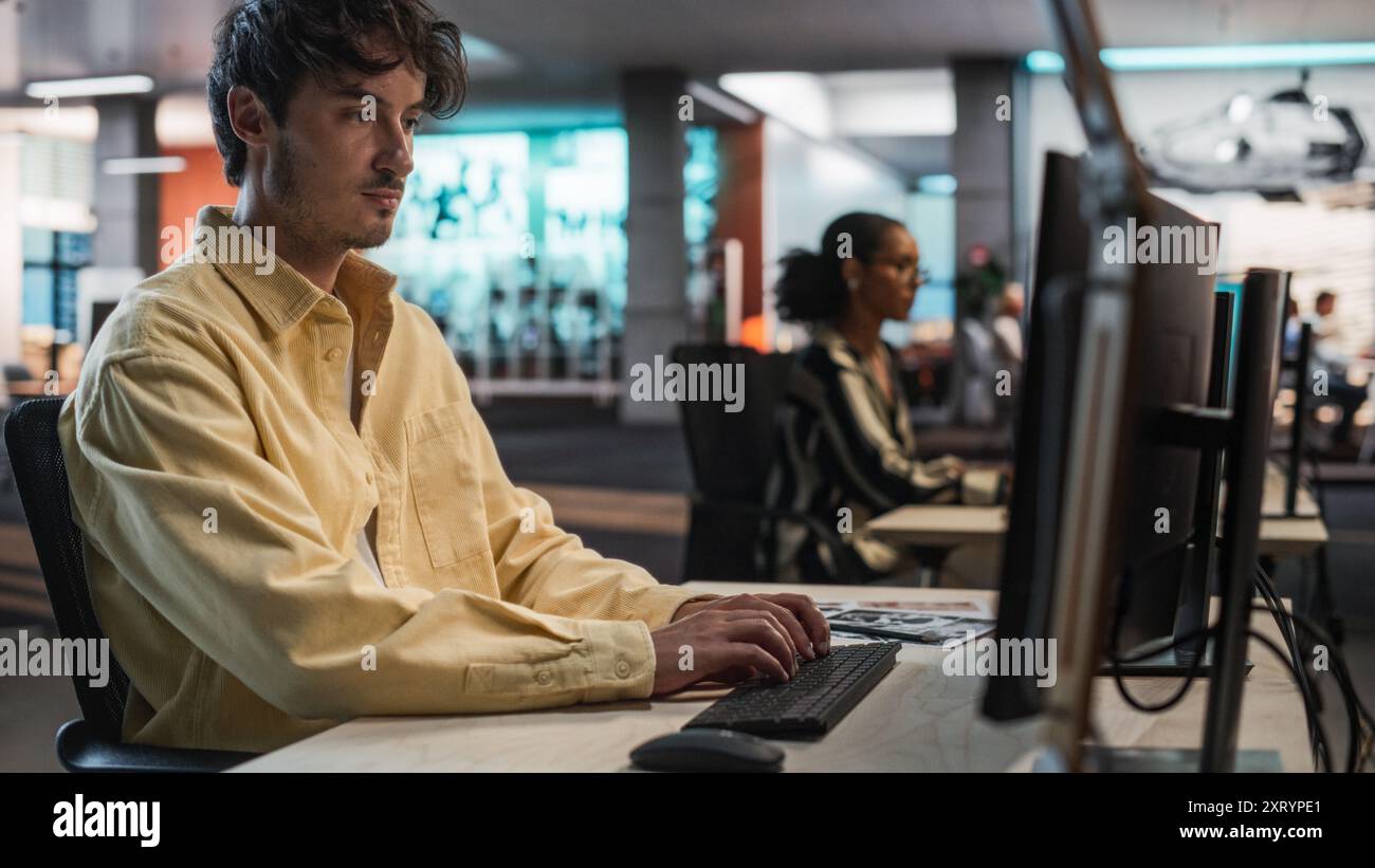 Programmeur de jeu caucasien masculin codage sur ordinateur de bureau dans Game Design Studio diverse Office. Focused Man écrit des lignes de code, fait de l'ingénierie de gameplay pour le nouveau jeu vidéo de survie immersive 3D. Banque D'Images