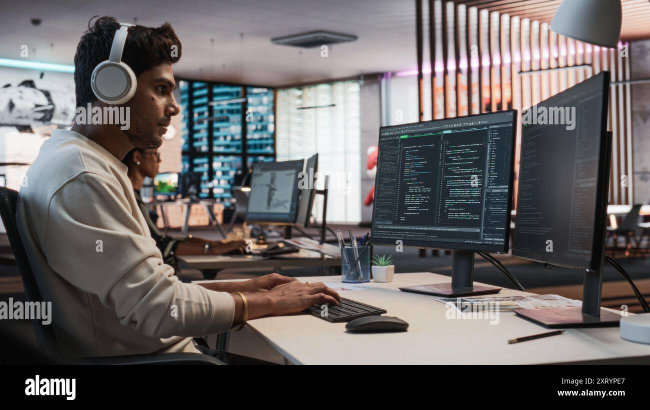 Programmeur de jeu indien masculin codage sur ordinateur de bureau dans Game Design Studio diverse Office. Focused Man écrit des lignes de code, fait de l'ingénierie de gameplay pour le nouveau jeu vidéo de survie immersive 3D. Banque D'Images