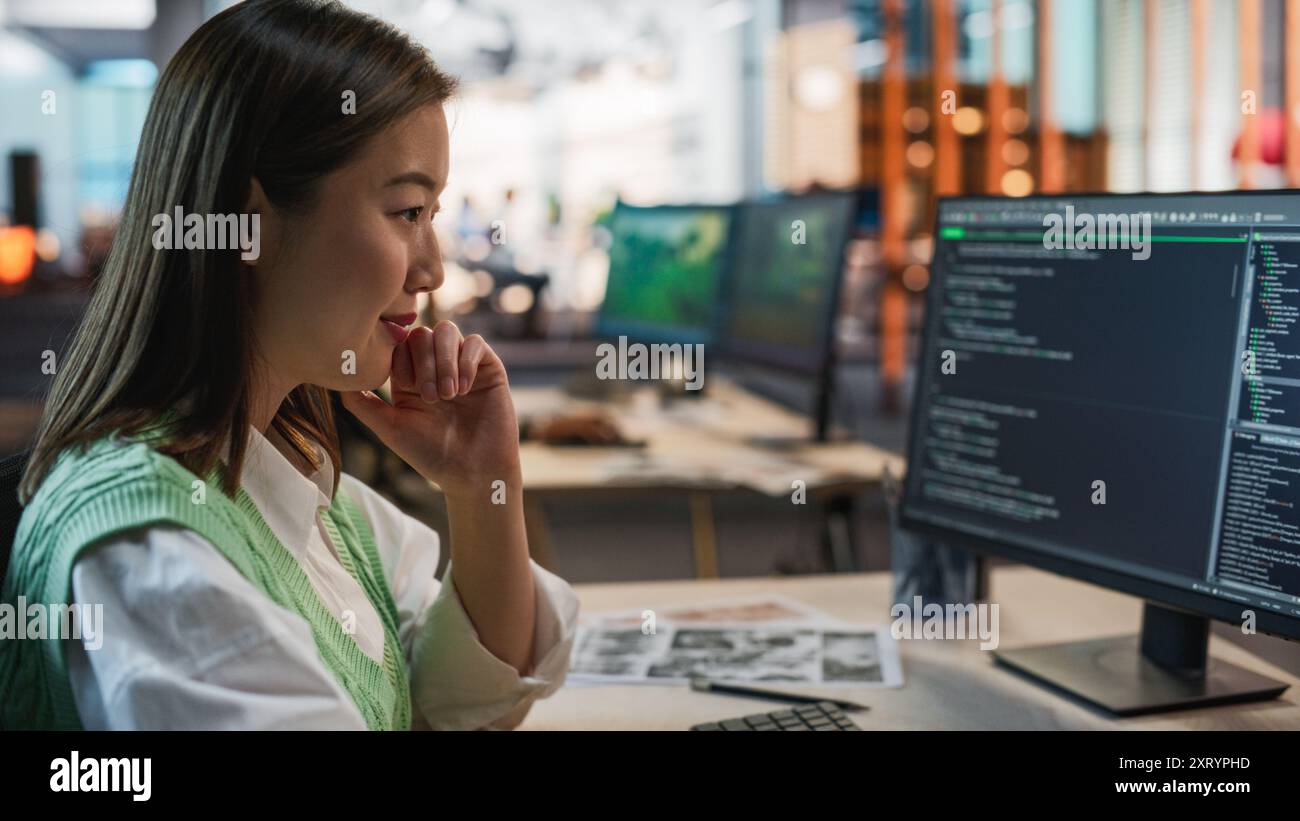 Programmeur de jeu asiatique féminin codage sur ordinateur de bureau dans Game Development Studio diverse Office. Focused Woman écrit des lignes de code, fait de l'ingénierie IA pour le nouveau jeu vidéo de survie 3D immersive Banque D'Images