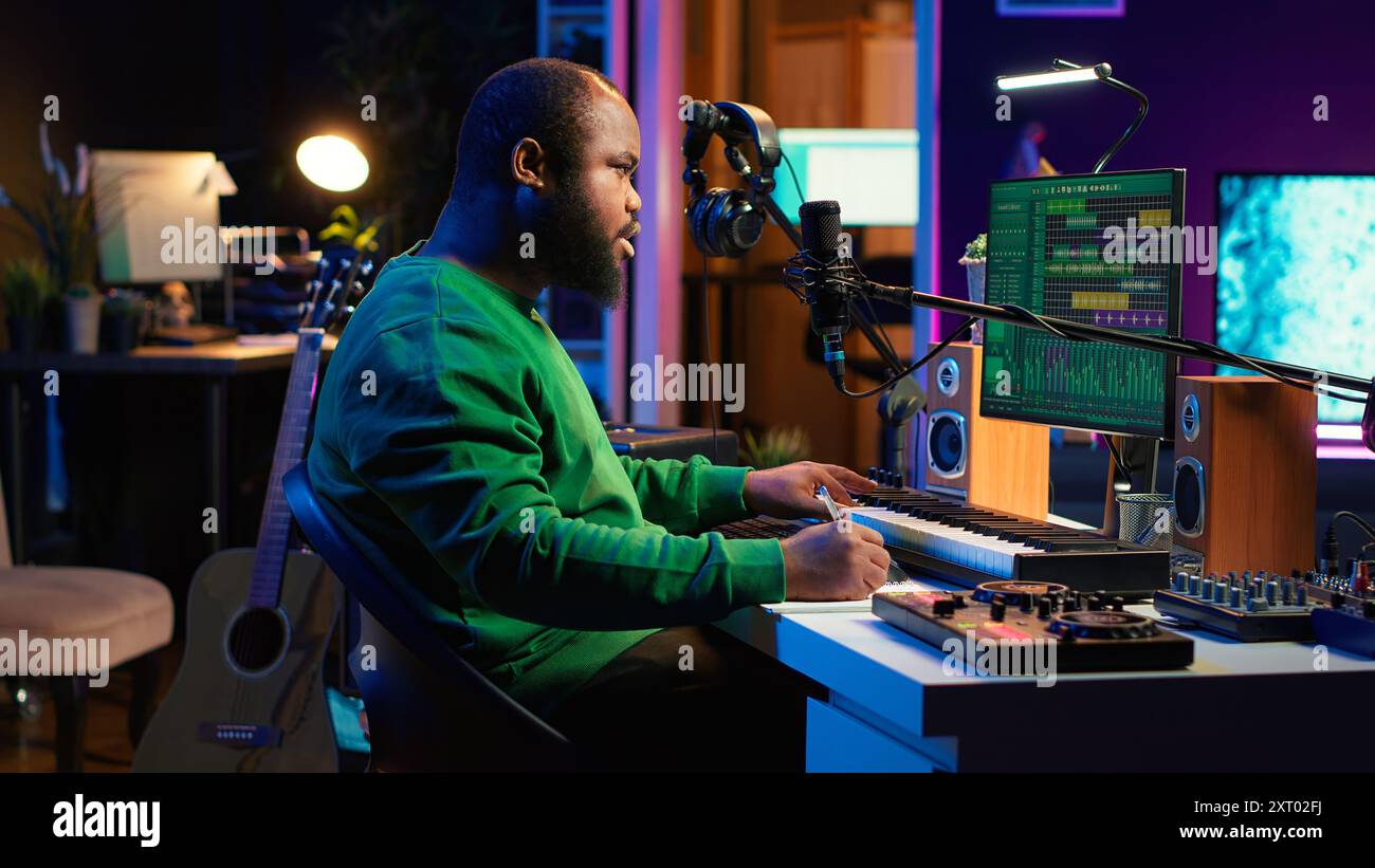 Auteur-compositeur prenant des notes pour créer de nouvelles pistes pour un album dans son home studio, écrivant des paroles et des éléments harmoniques avant d'enregistrer sa chanson et montage sur logiciel, ingénierie acoustique. Caméra A. Banque D'Images