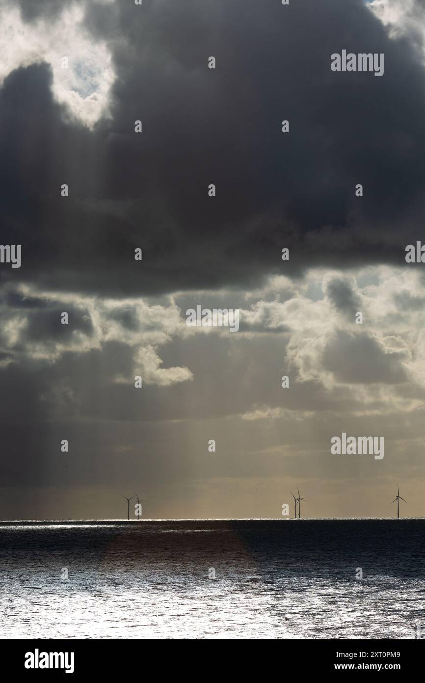 Nuages sombres d'un orage avec de la pluie tombant sur la mer du nord avec des silhouettes d'éoliennes en arrière-plan Banque D'Images