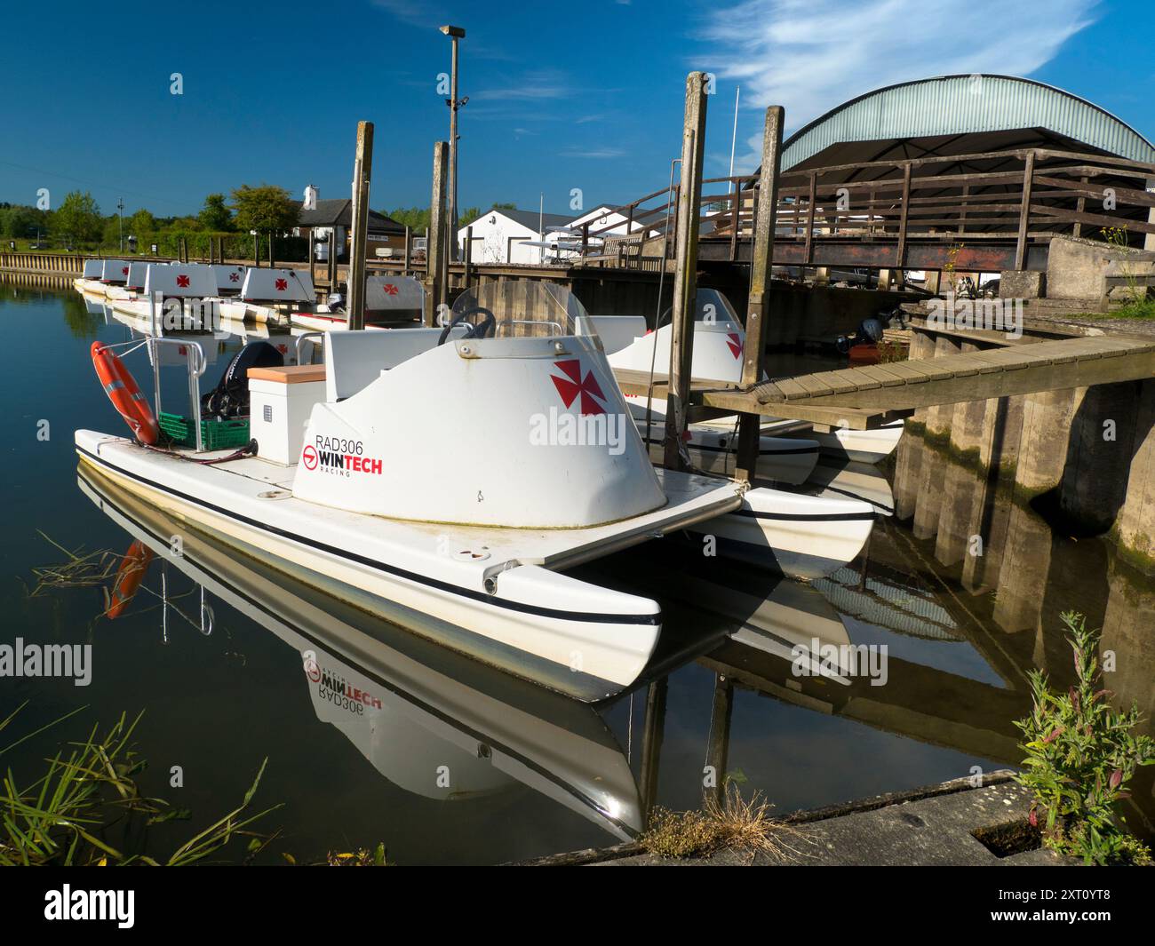 Fondé en 1921 et situé sur une belle partie de la Tamise dans l'Oxfordshire, Radley Boathouse sert Radley College et les amateurs d'aviron locaux depuis plus d'un siècle. Ici, nous voyons une ligne de bateaux de plaisance amarrés par sa jetée, tôt par un beau matin de printemps. Pourquoi la Croix de Malte ? C'est une longue histoire... Il a été adopté à l'origine par le Collège comme badge pour tous les sports vers 1850. Il est devenu le symbole du Boat Club à partir de la première équipe connue, et a probablement été adopté en l'honneur de Sir George Bowyer, le propriétaire de Radley Hall et à qui la maison et les terrains ont été loués quand t Banque D'Images