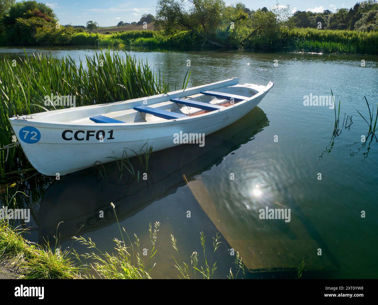 Fondé en 1921 et situé sur une belle partie de la Tamise dans l'Oxfordshire, Radley Boathouse sert Radley College et les amateurs d'aviron locaux depuis plus d'un siècle. Ici, nous voyons un bateau à rames amarré par sa jetée, tôt par un beau matin d'été. Il flotte au-dessus d'un compagnon submergé et coulé. Banque D'Images