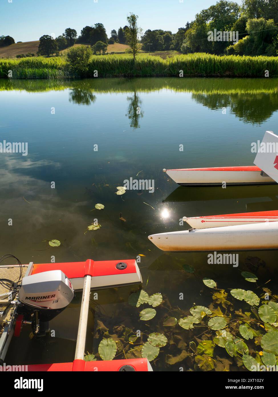 Fondé en 1921 et situé sur une belle partie de la Tamise dans l'Oxfordshire, Radley Boathouse sert Radley College et les amateurs d'aviron locaux depuis plus d'un siècle. Si vous vous tenez sur sa jetée et regardez à travers la rive nord de la rivière, vous verrez un arbre isolé et plutôt charmant, qui semble changer de caractère et d'apparence tout au long de l'année. Ici, nous le voyons par une belle et ensoleillée matinée d'été, avec les catamarans de plaisir omniprésents du hangar à bateaux au premier plan. La Croix de Malte rouge est l'emblème du club de navigation de l'université. Banque D'Images