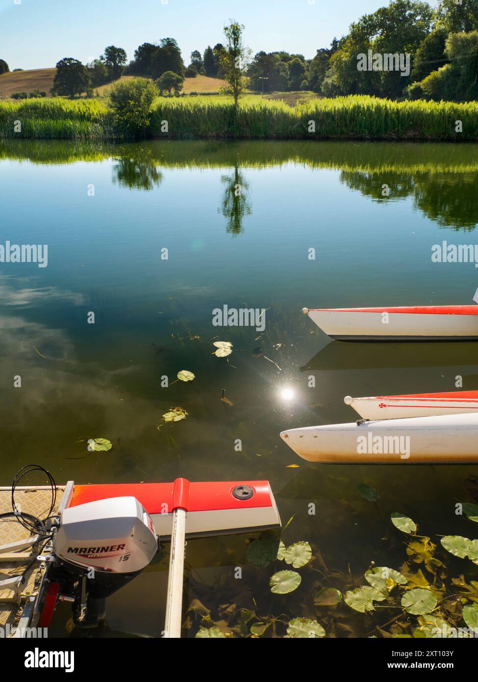 Fondé en 1921 et situé sur une belle partie de la Tamise dans l'Oxfordshire, Radley Boathouse sert Radley College et les amateurs d'aviron locaux depuis plus d'un siècle. Si vous vous tenez sur sa jetée et regardez à travers la rive nord de la rivière, vous verrez un arbre isolé et plutôt charmant, qui semble changer de caractère et d'apparence tout au long de l'année. Ici, nous le voyons par une belle et ensoleillée matinée d'été, avec les catamarans de plaisir omniprésents du hangar à bateaux au premier plan. La Croix de Malte rouge est l'emblème du club de navigation de l'université. Banque D'Images