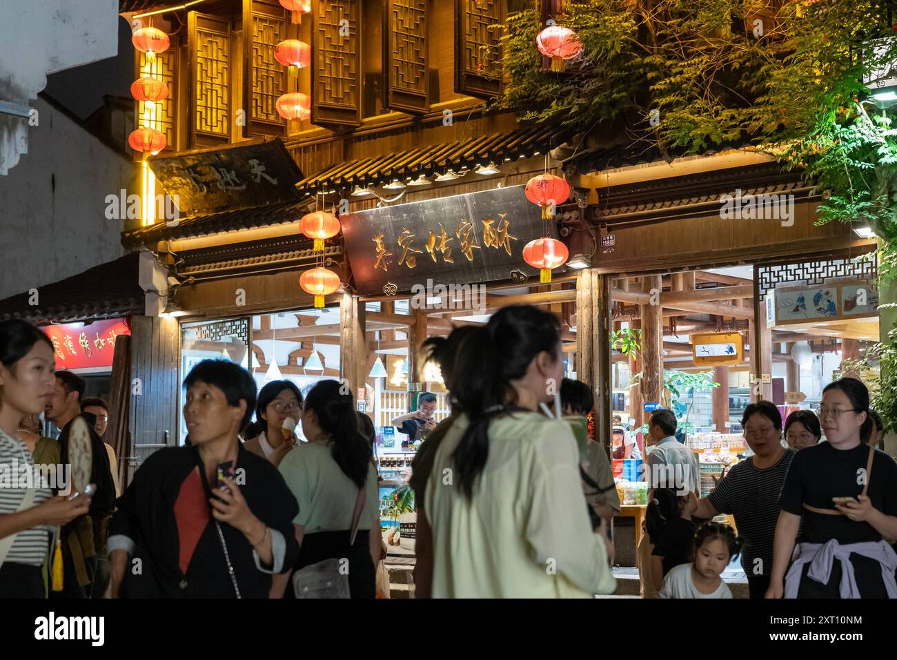 Suzhou, Chine - 11 juin 2024 : Une rue bondée à Suzhou, Chine la nuit, avec des lanternes rouges suspendues au-dessus d'une entrée de magasin. Banque D'Images