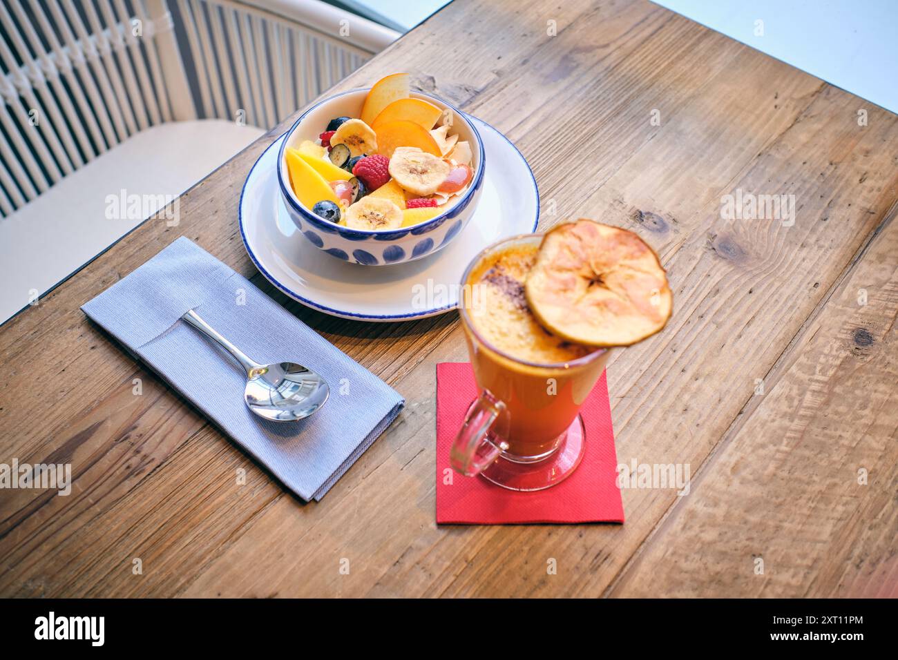 Une exposition vibrante de fruits mélangés dans un bol décoratif associé à un verre de boisson épicée, complétée par une cuillère en bois et une serviette en lin sur une rouille Banque D'Images