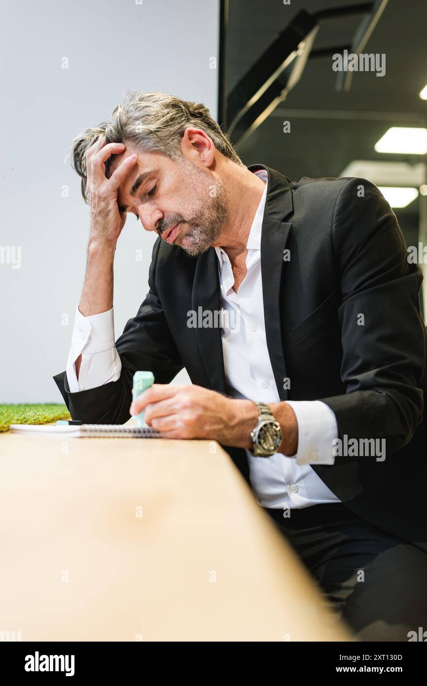 Un cadre pensif semble profond dans la pensée tout en examinant les notes, illustrant la concentration et la prise de décision dans un environnement de bureau Banque D'Images