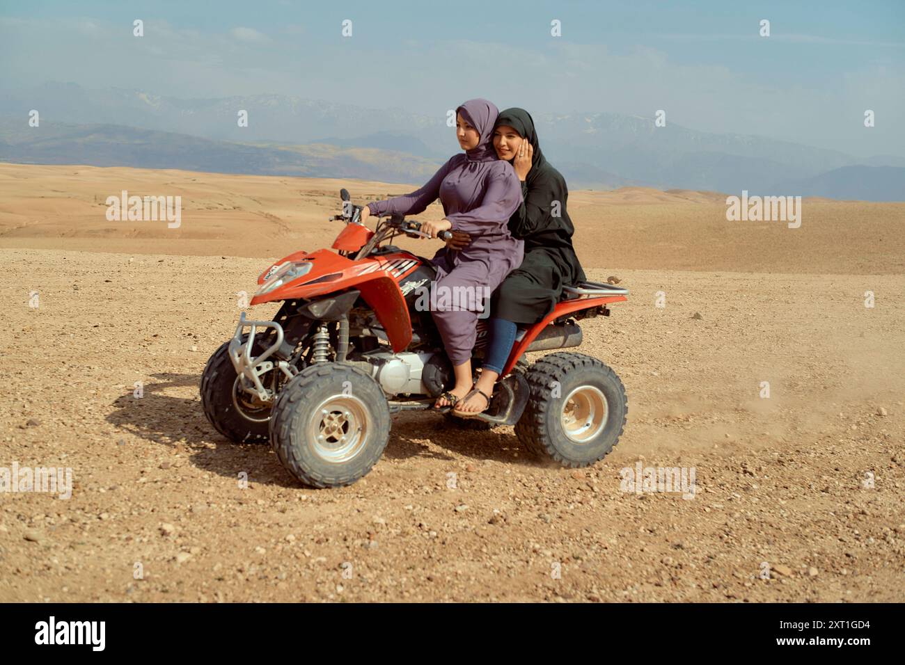 Deux jeunes filles souriantes assis sur un quad rouge dans un paysage désertique avec des montagnes en arrière-plan. Bola02562 Copyright : xConnectxImagesx Banque D'Images