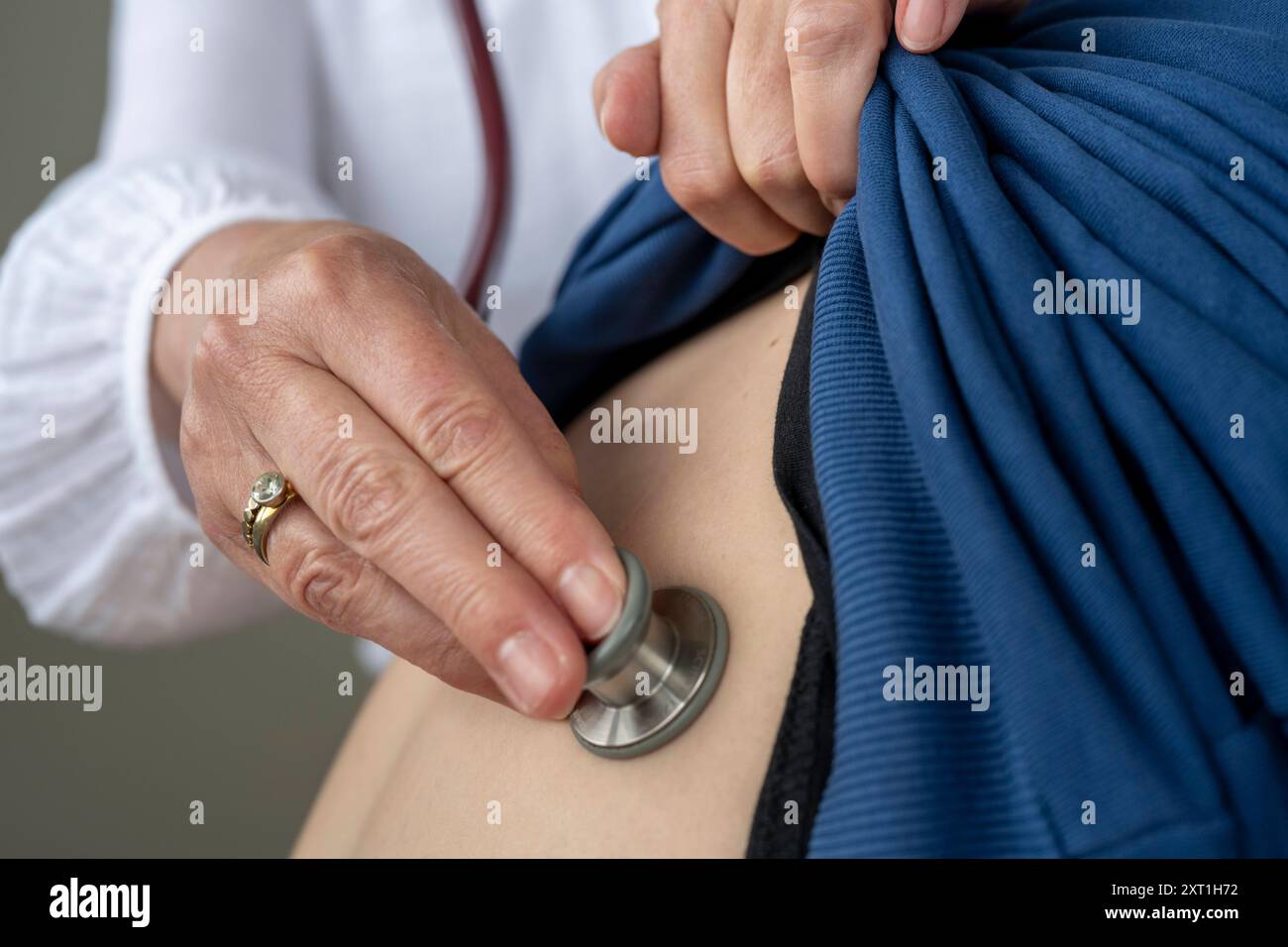 Diverse situatie in een huisartsenpraktijk Un médecin effectue un examen physique en utilisant un stéthoscope sur le dos d un patient, soulevant une chemise bleue Banque D'Images