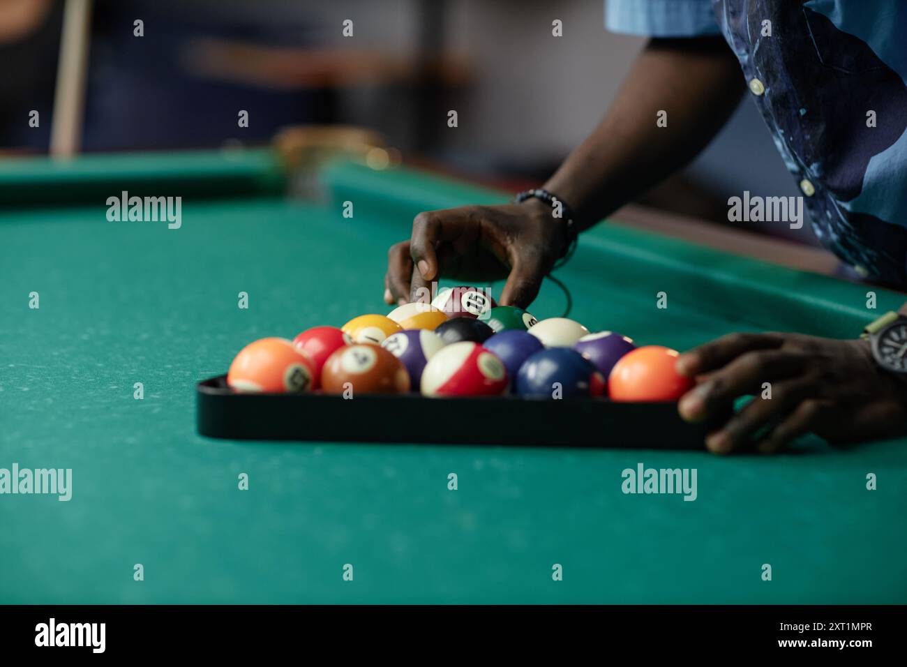 Gros plan des mains arrangeant des boules de billard colorées dans un rack triangulaire sur une table de billard verte dans une pièce faiblement éclairée capturant l'essence de la préparation du jeu Banque D'Images