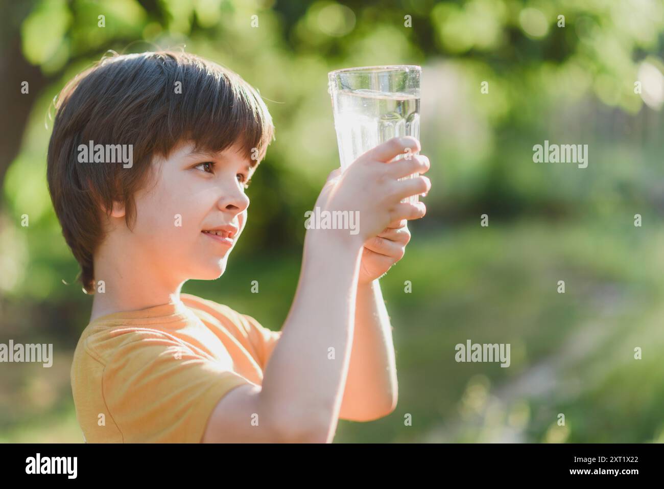 Un beau garçon tient un verre d'eau propre dans sa main dans la nature par une journée ensoleillée Banque D'Images