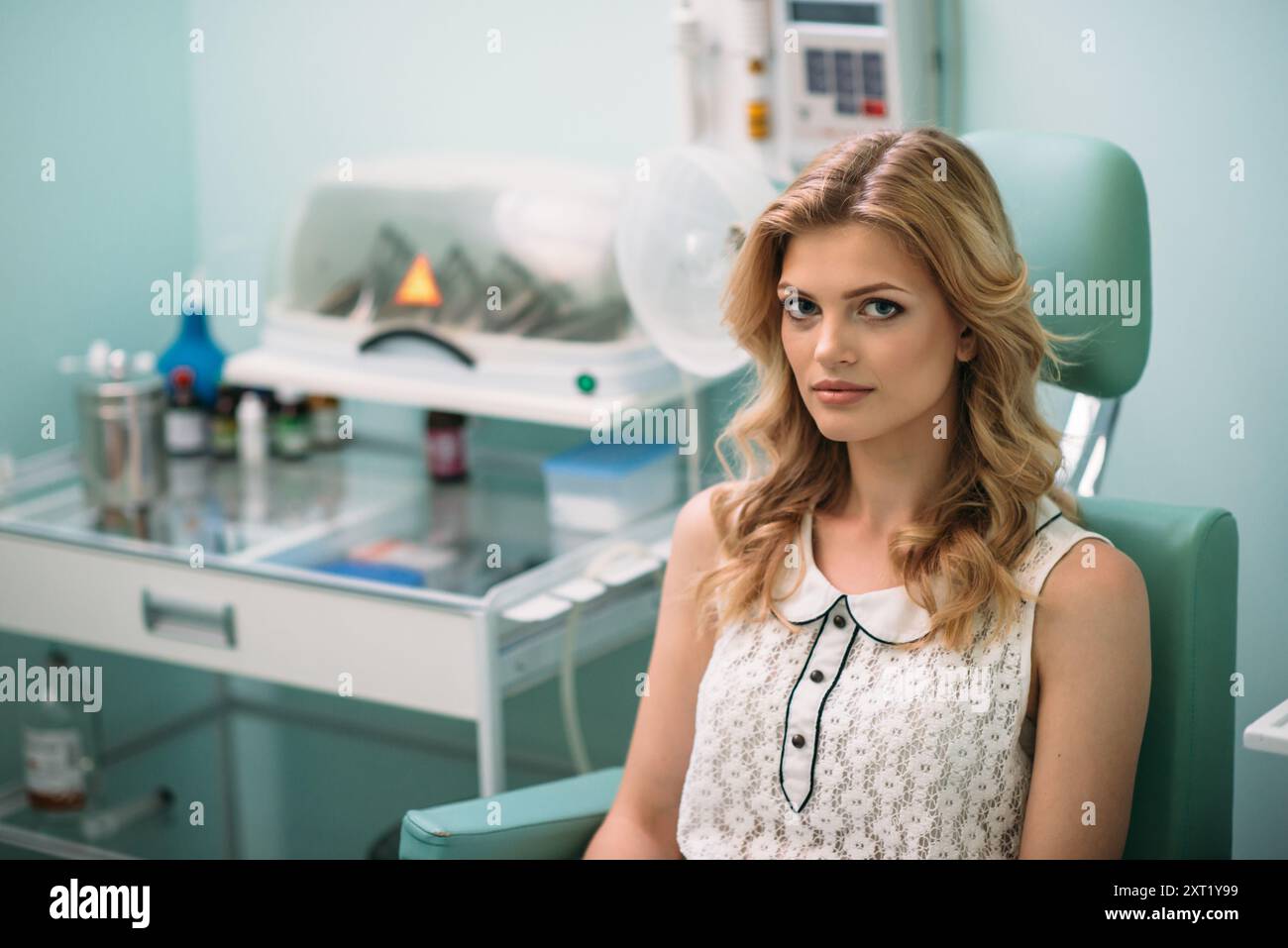 Une jeune femme aux cheveux ondulés attend calmement dans une clinique dentaire, entourée de matériel dentaire et d’une ambiance paisible. Banque D'Images