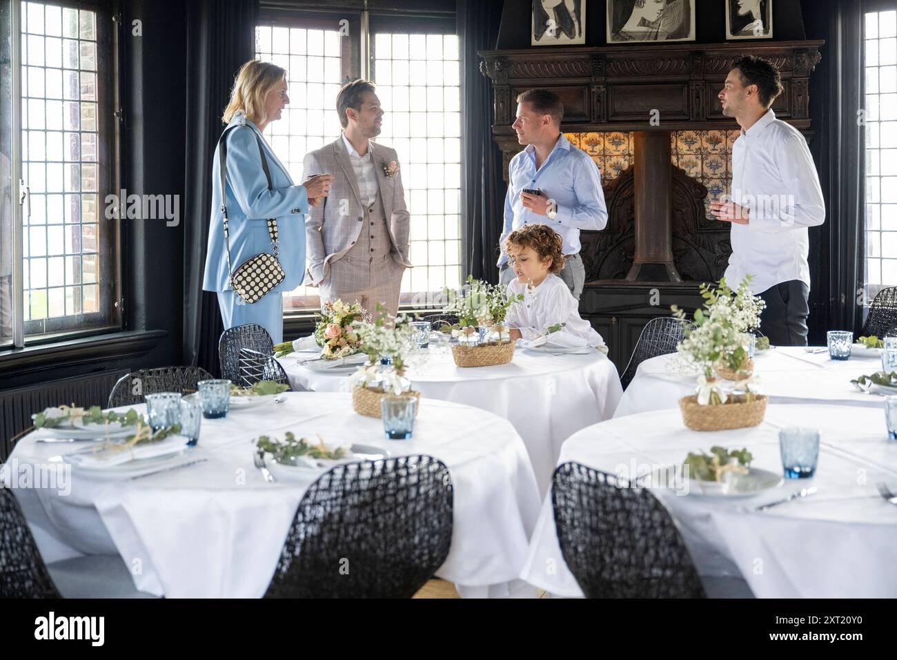 Salle à manger élégante avec des invités bien habillés engagés dans la conversation, avec une table ornée de pièces maîtresses de fleurs blanches. Panc05811 copie Banque D'Images