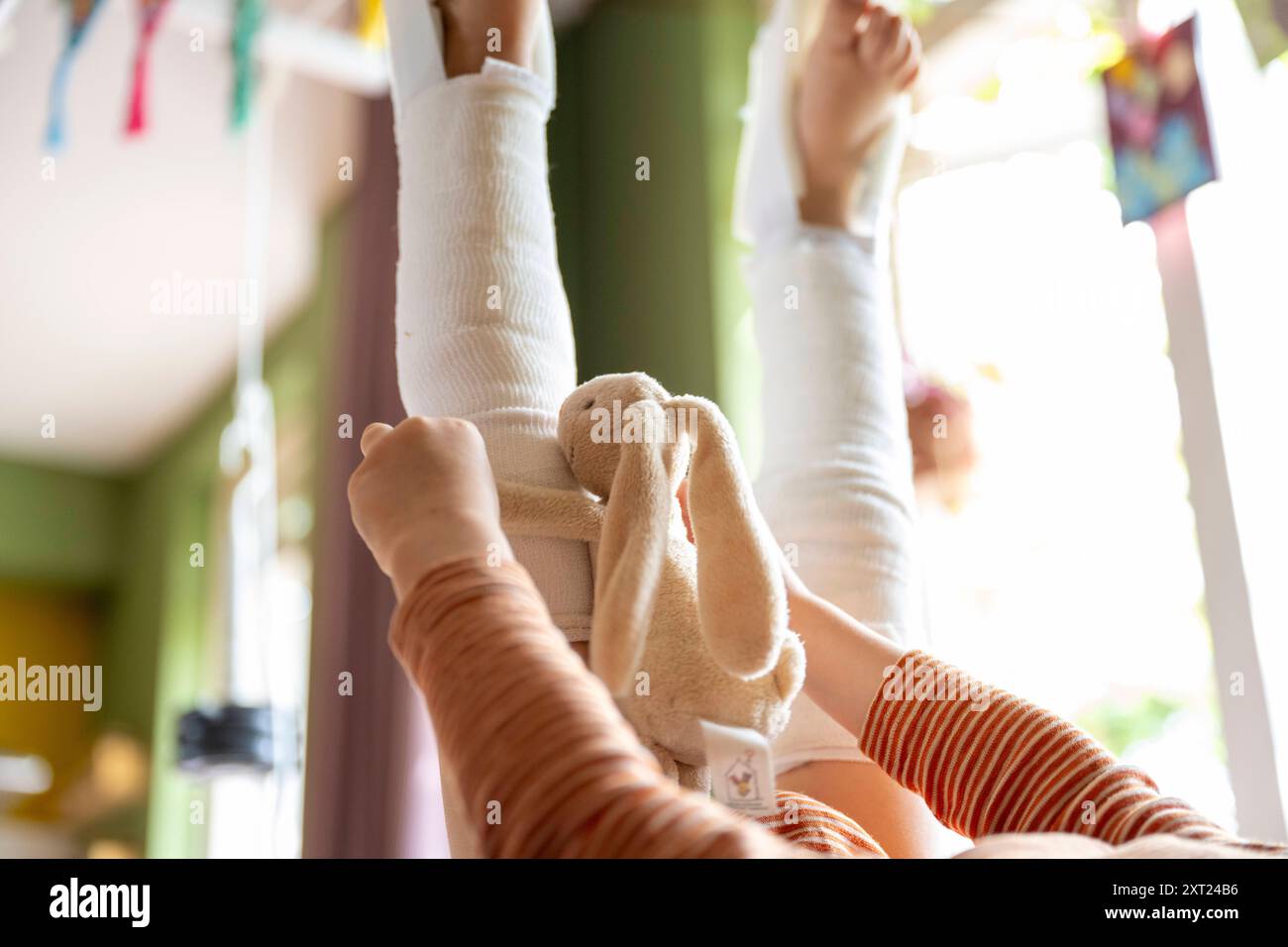 Enfant allongé sur le dos tenant un lapin en peluche, avec les pieds relevés en l'air portant des chaussettes rayées. Panc06146 Copyright : xConnectxImagesx Banque D'Images