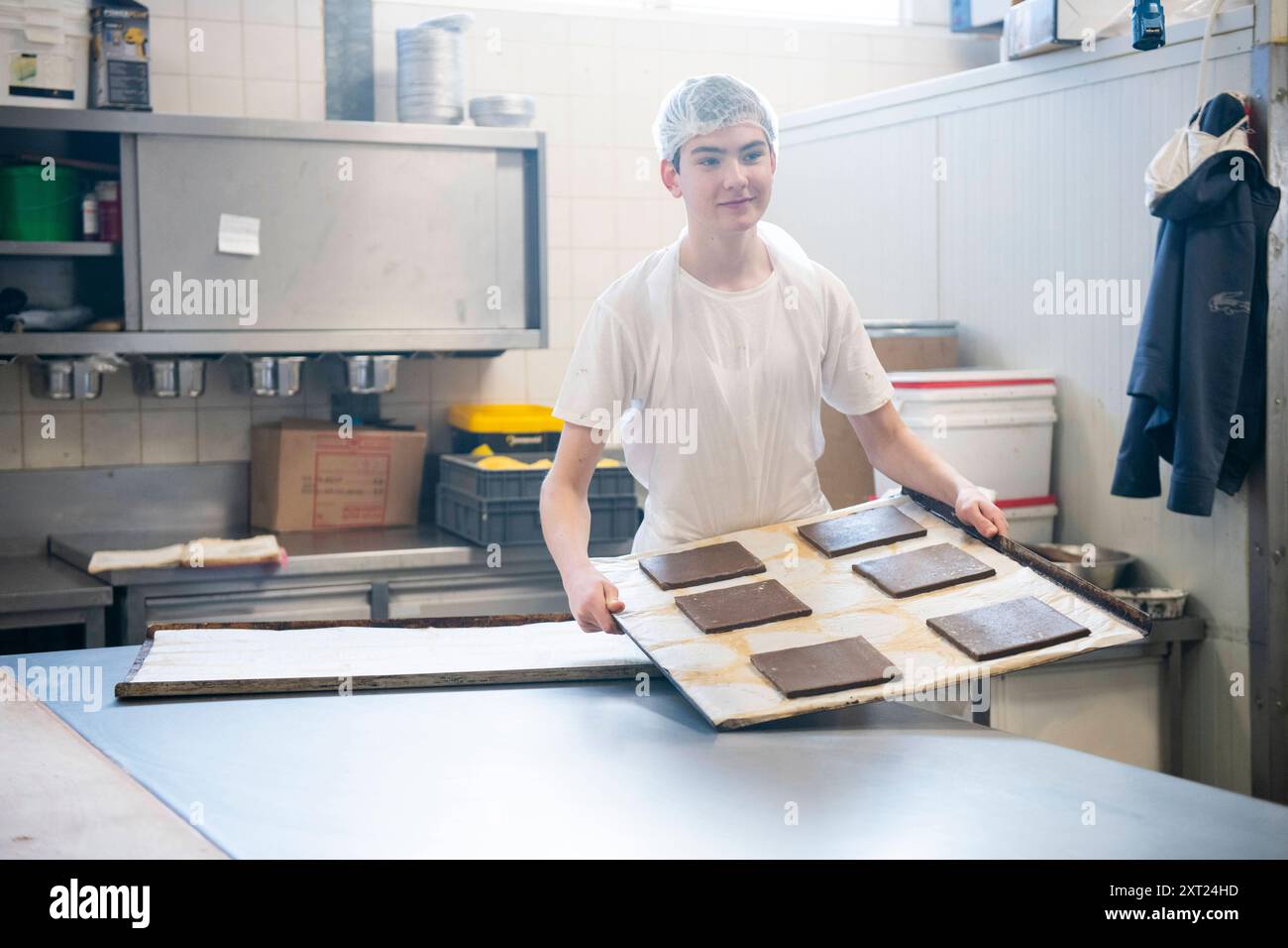 Banketbakkerij Un boulanger souriant dans un t-shirt blanc porte un grand plateau de brownies frais dans une cuisine professionnelle. Molenhoek Nederland panc06194 copie Banque D'Images