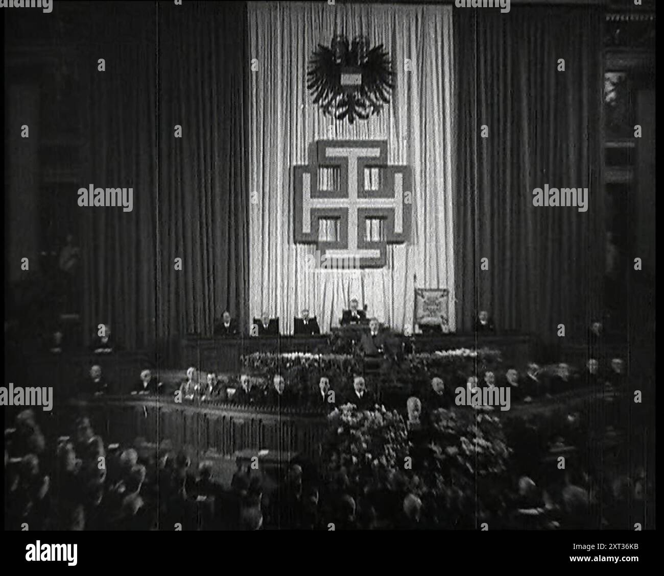 La salle de débat du Parlement à Vienne pendant l'annexion nazie allemande de l'Autriche, avec des politiciens remplissant la salle en écoutant Kurt Schusschnigg, le chancelier autrichien, au Lectern et les hauts fonctionnaires sur le Dais derrière lesquels se trouvent des rideaux dans le rouge et blanc du drapeau autrichien sur lesquels sont montés un symbole d'aigle à double tête et la croix le Parti 'Front patrie', 1938. De "Time to Remember - Wind Up week", 1938 (bobine 1) ; film documentaire sur 1938 - les gens prennent conscience de la menace croissante de la guerre. Banque D'Images