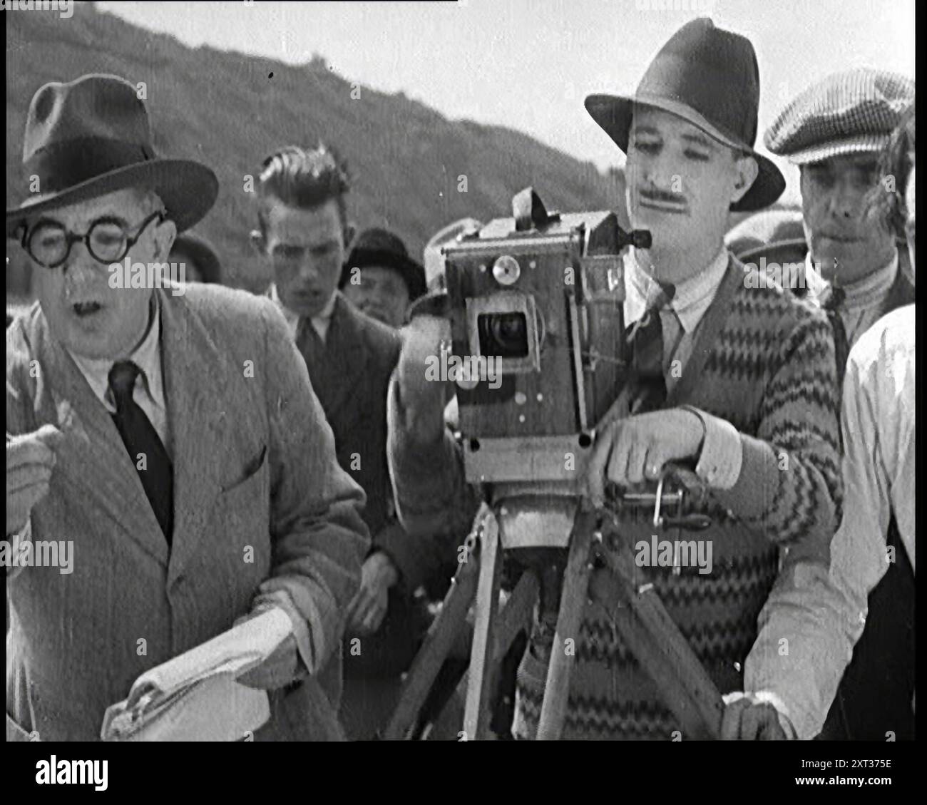Un caméraman masculin manœuvrant une caméra sur un plateau de film comme le réalisateur masculin instruit des acteurs, des années 1920 Tournage en lieu et place. '...Elstree [studios de cinéma] à l'époque des silences...quand le temps était beau bien sûr, au soleil nous sommes allés'. De "Time to Remember - came the Dawn", 1925 (bobine 1) ; aperçu de l'industrie cinématographique britannique des années 1920 - extraits de grands films muets et de nouvelles. Banque D'Images