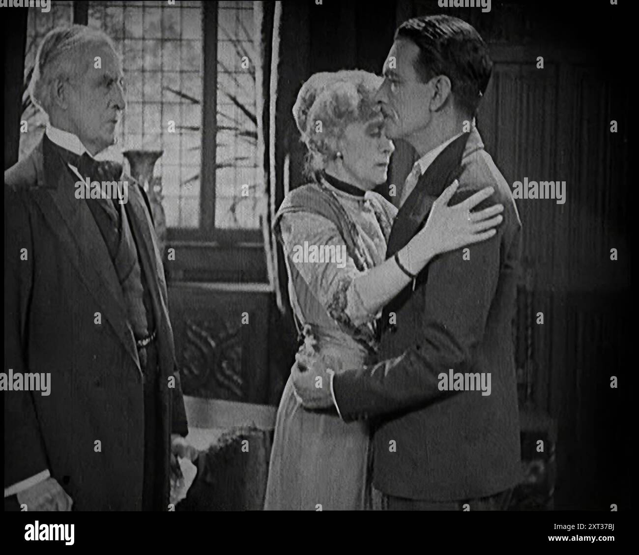 Extrait d'un film silencieux. Un acteur féminin et un acteur masculin embrassent. Un autre acteur masculin regarde, 1920s. «... nous avons créé notre fabrication de celluloïd non pas avec un écran large et un discours stéréophonique argenté, mais avec un simple mime et un silence doré ». De "Time to Remember - came the Dawn", 1925 (bobine 1) ; aperçu de l'industrie cinématographique britannique des années 1920 - extraits de grands films muets et de nouvelles. Banque D'Images