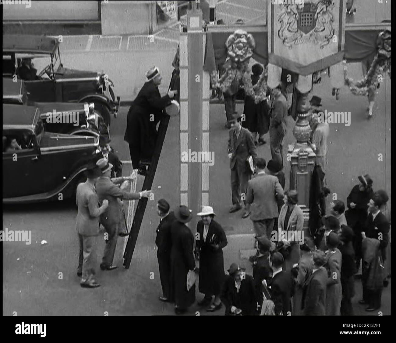 Bud Flanagan avec une poêle à frire grimpant une échelle reposant contre les décorations du couronnement dans Oxford Street tandis que les passants regardent, et Chesney Allen grimpe derrière lui avec un troisième homme, 1937 ans. « Dernières touches aux décorations [à Londres]. Mais qui est-ce qui met leur rame - ou plutôt leur échelle - dedans? [Duo comique] Flanagan et Allan, ayant découvert que certains des postes supportent des torches, décident d'économiser des factures de carburant en faisant leur cuisine à Oxford Street. De "Time to Remember - Sense of Values", 1937 (Reel 2) ; film documentaire sur les événements de 1937, la guerre dans les lointains EA Banque D'Images