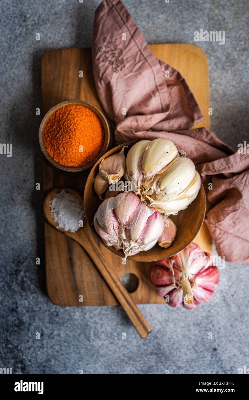 Une scène culinaire rustique avec des bulbes d'ail entiers disposés artistiquement sur une planche de bois, accompagnés d'un bol d'épices orange vibrantes et d'une épingle Banque D'Images