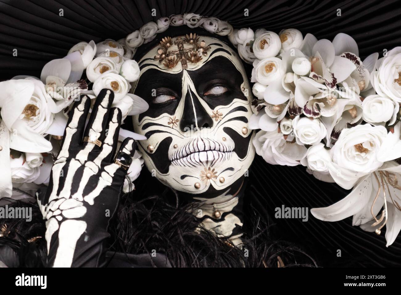 Une image frappante d'une femme ornée d'un maquillage traditionnel Day of the Dead, avec un motif semblable à un crâne, entouré d'un somptueux arrangement de blanc Banque D'Images