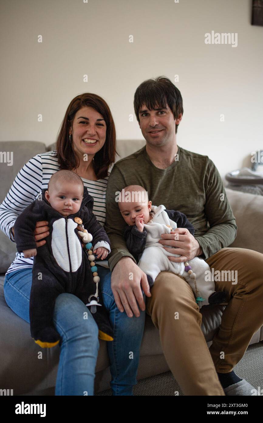 Une famille joyeuse de quatre personnes, composée de parents et de jumeaux, profite d'un moment ensemble sur un canapé dans un environnement chaleureux et accueillant Banque D'Images