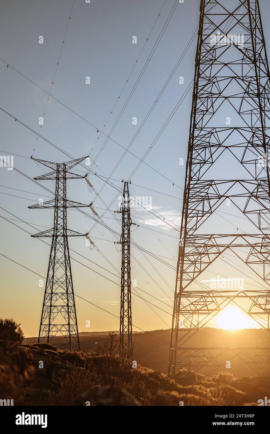Les tours de transmission d'énergie se dressent face à un coucher de soleil doré dans l'Espagne rurale, mettant en valeur l'infrastructure d'une centrale hydroélectrique. Banque D'Images