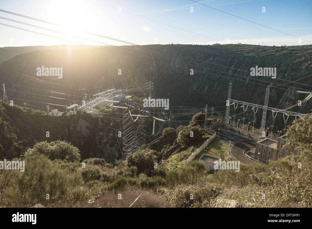 Capturée dans la lueur chaude de la lumière du soleil, cette image montre une centrale hydroélectrique sereine nichée dans la colline espagnole, avec une ligne haute tension Banque D'Images