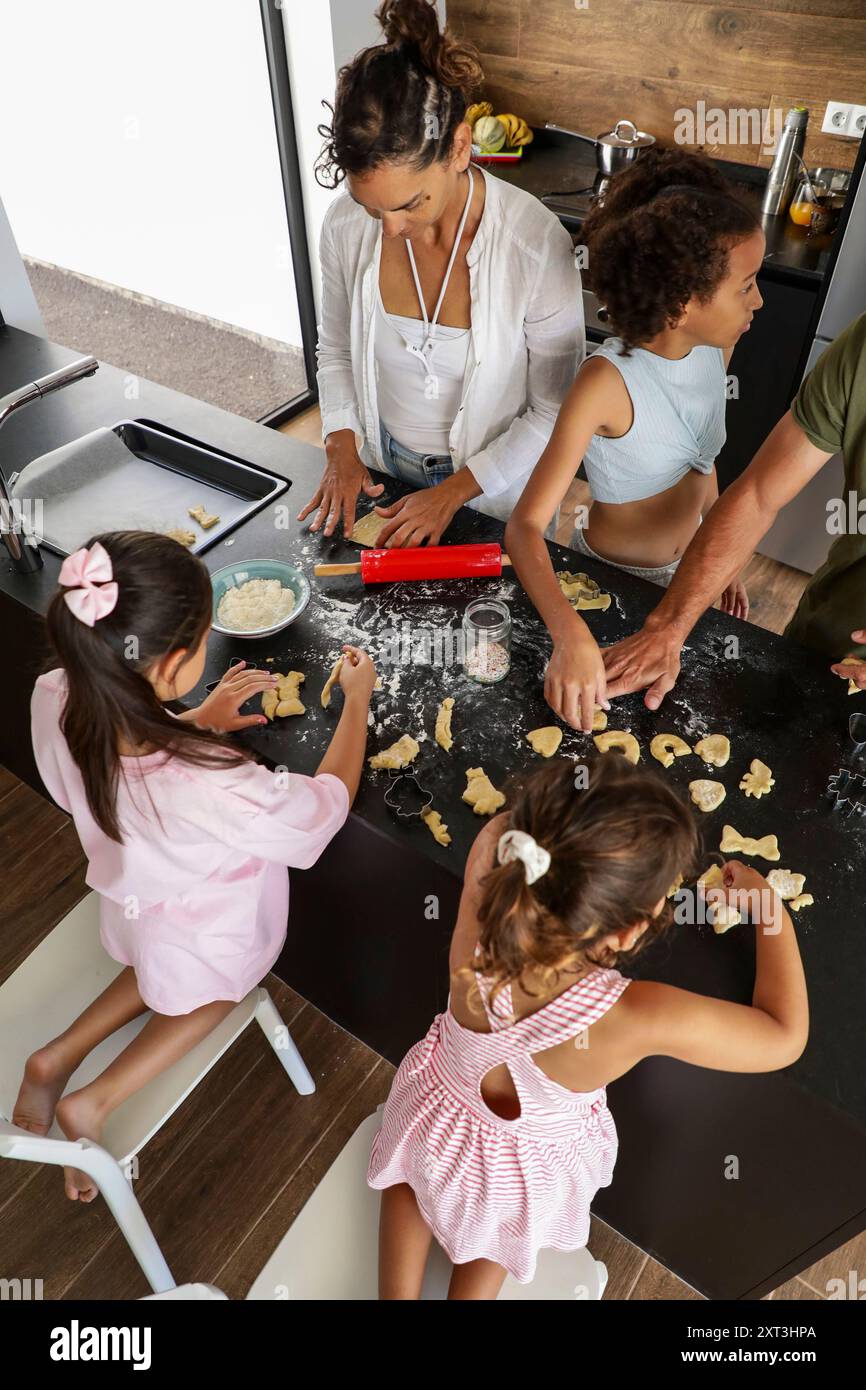 Une famille aime cuire des biscuits ensemble, façonner la pâte sur un comptoir de cuisine en désordre centré sur l'interaction et le travail d'équipe dans un cadre confortable à la maison Banque D'Images
